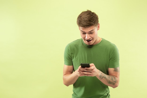 Foto grátis retrato de meio comprimento de jovem caucasiano sobre fundo verde do estúdio. lindo modelo masculino na camisa. conceito de emoções humanas, expressão facial, vendas, anúncio. apostas, compras online, navegação na web.