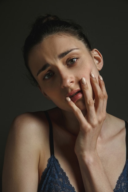 Retrato de meio corpo de jovem triste em roupa interior na parede escura do estúdio