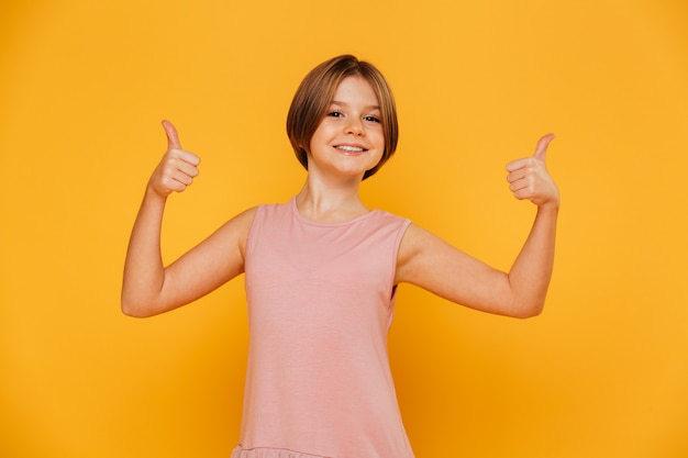 Retrato de menina alegre, sorrindo e mostrando os polegares para cima isolado