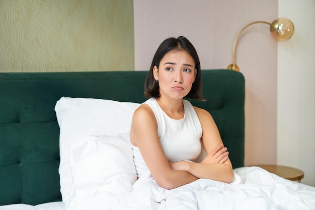 Foto grátis retrato de menina asiática na cama parecendo complicada e preocupada cruzando os braços no peito franzindo a testa com unea