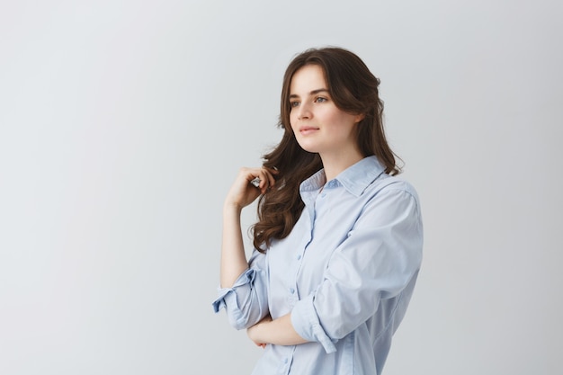 Retrato de menina bonita feminina com cabelo longo ondulado escuro, olhando de lado com expressão relaxada e calma. Copie o espaço.