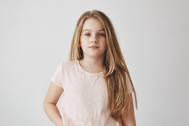 Retrato de menina bonita loira com cabelos longos, de pijama rosa. Criança acordou cedo, se preparando para a escola com expressão sonolenta.