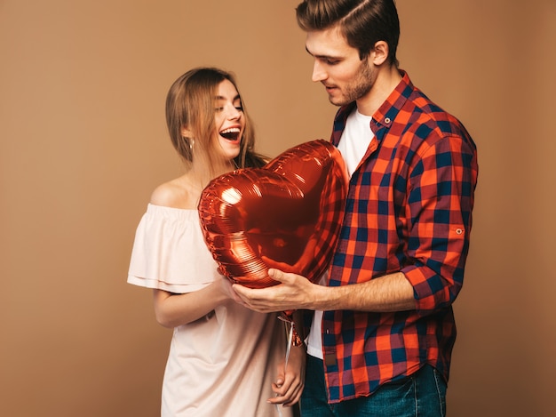 Retrato de menina bonita sorridente e seu namorado bonito segurando balões em forma de coração e rindo. Casal feliz no amor. Feliz Dia dos namorados