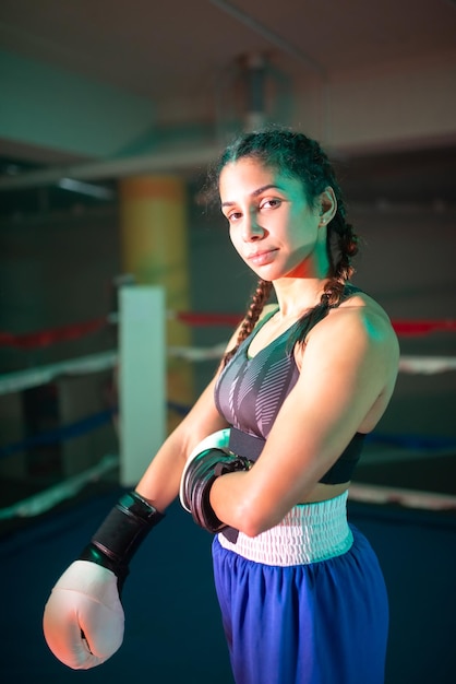 Retrato de menina boxer desportiva posando para a câmera. muito jovem em roupas esportivas e luvas de pé no anel no ginásio e orgulhosamente olhando para a câmera. boxe feminino, hobby e conceito de estilo de vida saudável