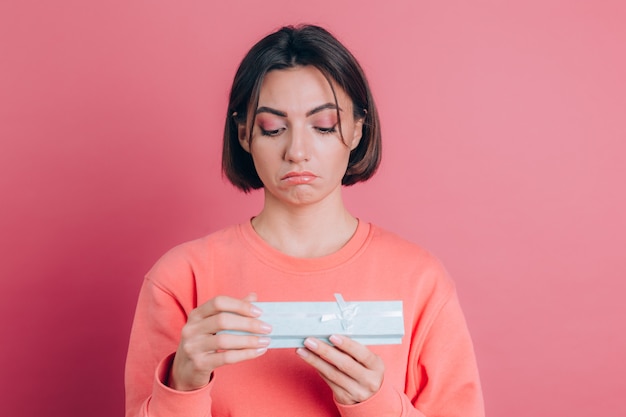 Retrato de menina chateada e frustrada abrindo uma caixa de presente isolada em um fundo rosa