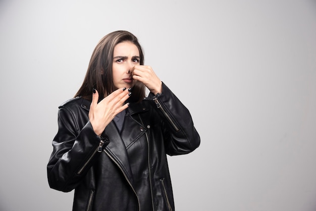 Retrato de menina em pé de jaqueta de couro preta estilo casual apertando o nariz