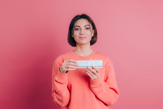 Retrato de menina feliz e sorridente abrindo uma caixa de presente isolada em um fundo rosa