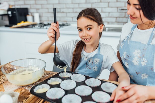 Retrato de menina feliz fazendo cupcakes com a mãe