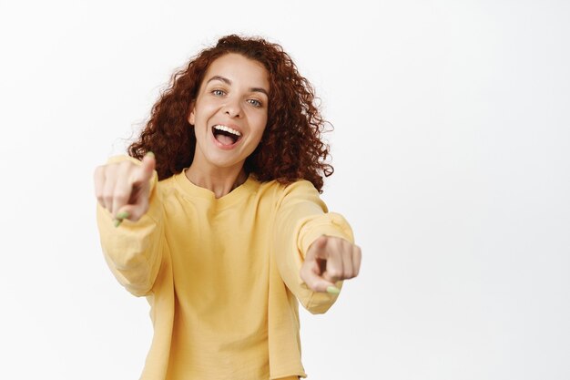 Retrato de menina feliz rindo apontando os dedos, sorrindo alegre, escolhendo você, escolhendo, convidando para trabalhar para empresa, parabenizando, em pé no branco.