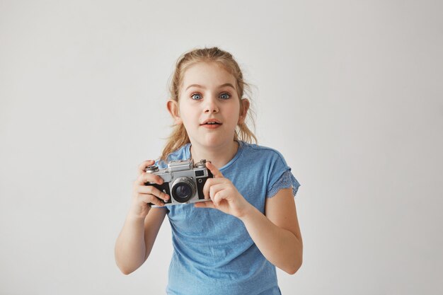 Retrato de menina loira bonita de camiseta azul, segurando a câmera nas mãos com expressão concentrada, indo tirar uma foto de gato bonito na rua.