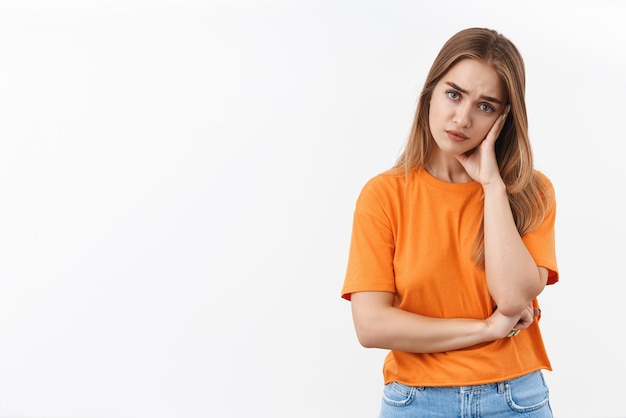 Retrato de menina loira perturbada e irritada cansada de ouvir as mesmas velhas mentiras e desculpas, apoiando-se na palma da mão e olhando cético com expressão entediada incomodada em pé de fundo branco