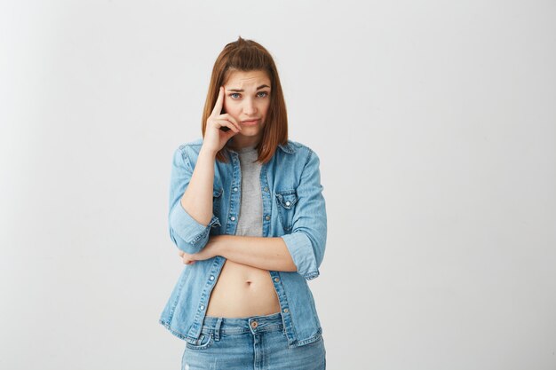 Retrato de menina morena jovem descontente com o dedo no pensamento do templo.