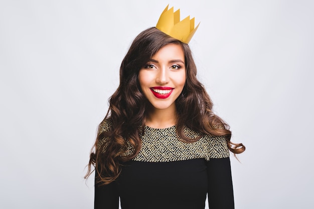 Retrato de menina muito positiva em vestido de moda com cabelo castanho longo encaracolado em coroa amarela no espaço em branco