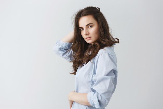 Retrato de menina na moda jovem estudante com cabelos ondulados escuros com olhar relaxado e confiante, posando para o ensaio fotográfico de moda.