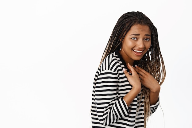 Retrato de menina negra feliz aponta para si mesma ri e sorri com expressão de rosto de descrença surpresa fica de perfil contra fundo branco