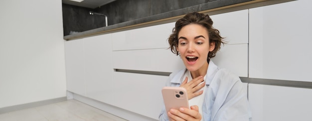 Retrato de menina olhando para a tela do telefone com rosto espantado mulher lendo notícias no smartphone com