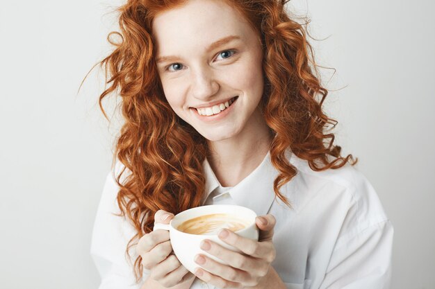 Retrato de menina ruiva macia com sardas sorrindo segurando xícara