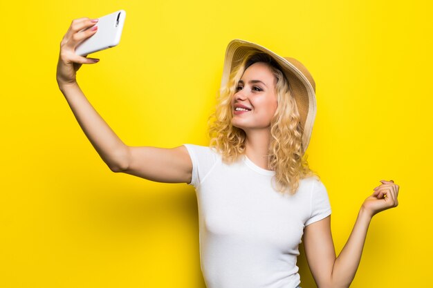 Retrato de menina tendo videochamada com amante, segurando o telefone inteligente na mão, fotografando selfie isolada na parede amarela. Aproveitando as férias de fim de semana