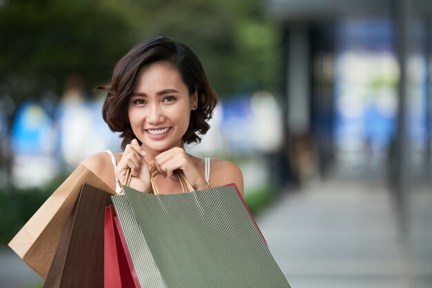 Retrato de menina viciada em compras adorável em pé com uma pilha de sacos de loja ao ar livre