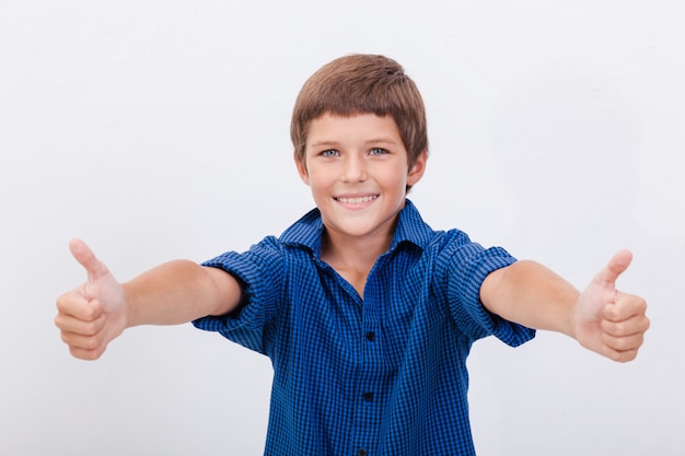 Retrato de menino feliz, mostrando os polegares para cima gesto