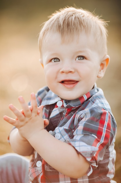 Foto grátis retrato de menino feliz sentado e batendo palmas enquanto desfruta do ar livre de férias. conceito de infância