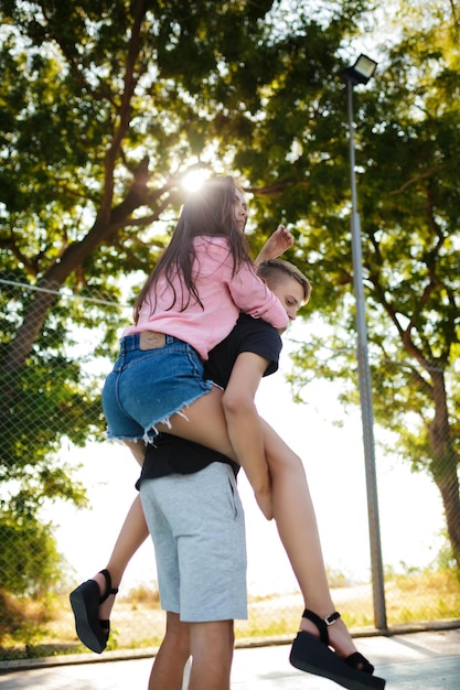 Retrato de menino segurando uma linda garota nas costas e se divertindo enquanto passam o tempo juntos no parque