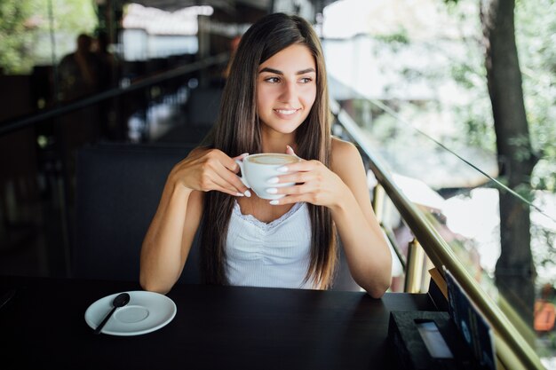 Retrato de moda ao ar livre de linda jovem bebendo chá e café