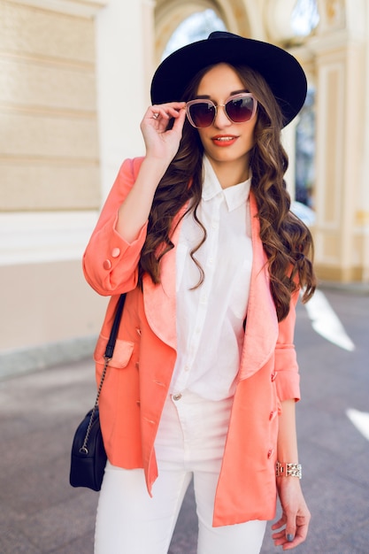 Retrato de moda hight ao ar livre de mulher casual elegante sexy chapéu preto, terno rosa, blusa branca posando na rua velha