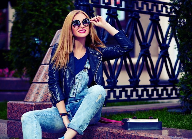 Retrato de modelo bonito engraçado moderno sexy urbano jovem mulher sorridente menina elegante pano moderno brilhante ao ar livre, sentado no parque em jeans em um banco em copos