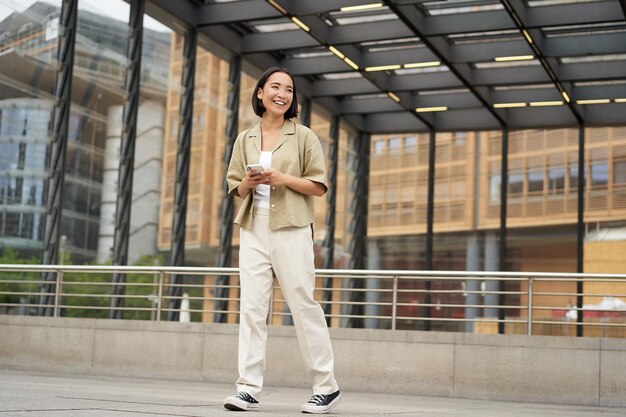 Retrato de modelo feminino asiático com telefone jovem coreana segurando smartphone na rua usando t