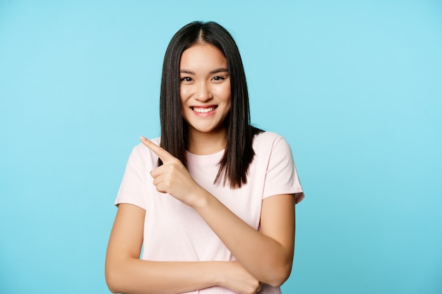 Retrato de modelo feminino asiático sorridente feliz apontando para o canto superior esquerdo, mostrando a loja de banner de venda.