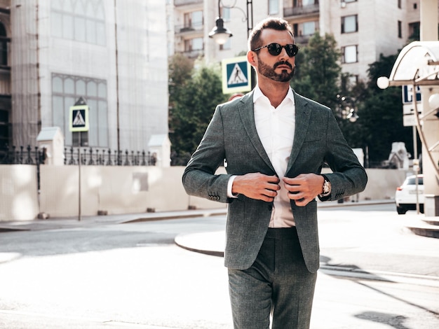 Retrato de modelo lambersexual de hipster elegante confiante bonito Homem moderno sexy vestido de terno elegante Moda masculina posando no fundo da rua na cidade da Europa ao pôr do sol em óculos de sol