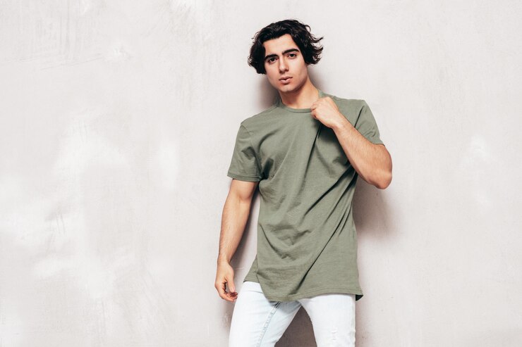 Foto grátis retrato de modelo lambersexual de hipster elegante e confiante bonito homem sexy vestido de tamanho grande, camiseta e jeans moda masculina isolada no estúdio posando perto da parede cinza