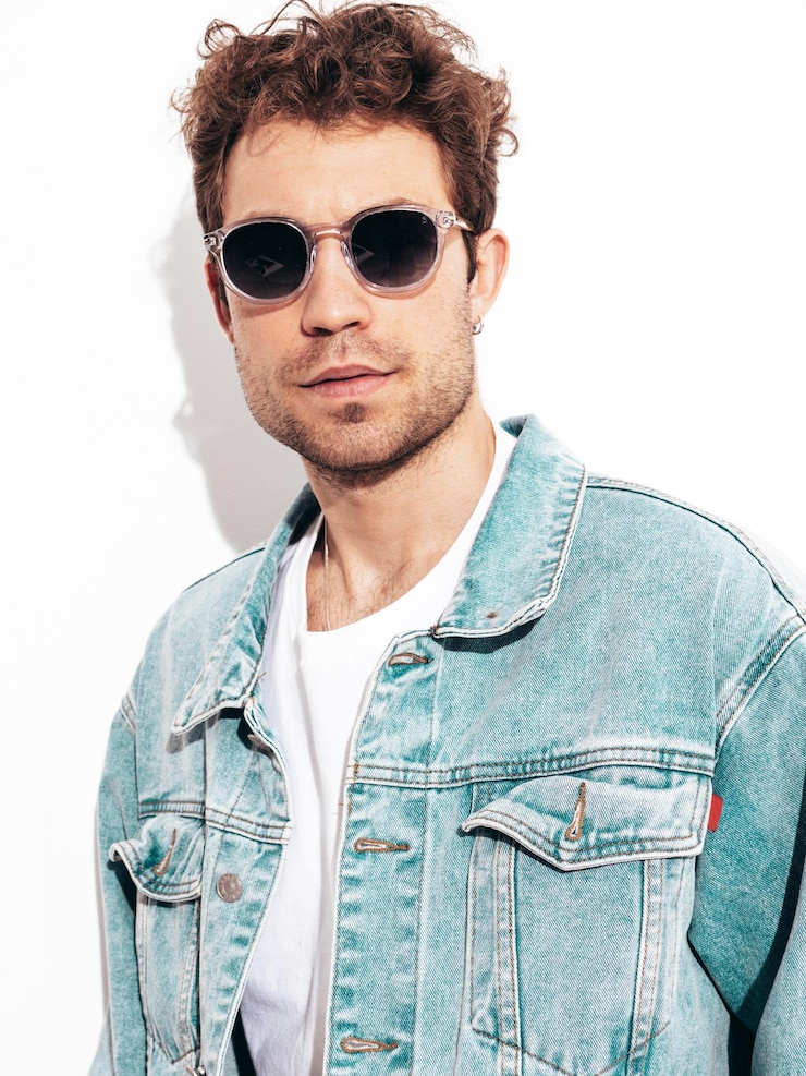 Foto grátis retrato de modelo lambersexual hipster elegante confiante bonito com penteado encaracolado homem sexy vestido com jaqueta jeans moda masculina isolada na parede branca no estúdio em óculos de sol