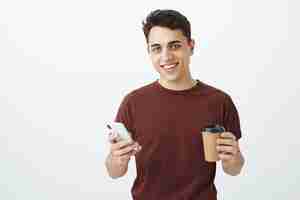 Foto grátis retrato de modelo masculino bonito despreocupado em camiseta vermelha com smartphone e xícara de café