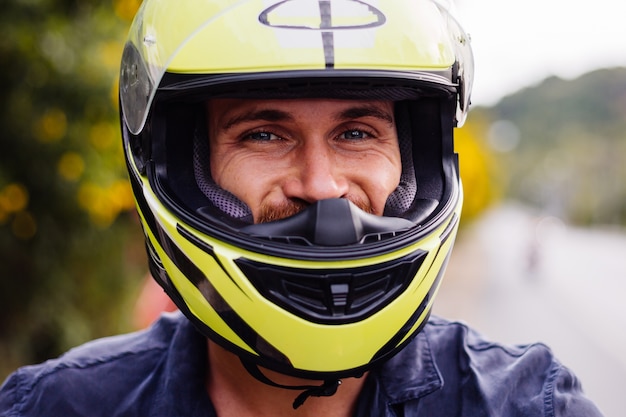 Retrato de motociclista com capacete amarelo em motocicleta na beira de uma estrada movimentada na Tailândia