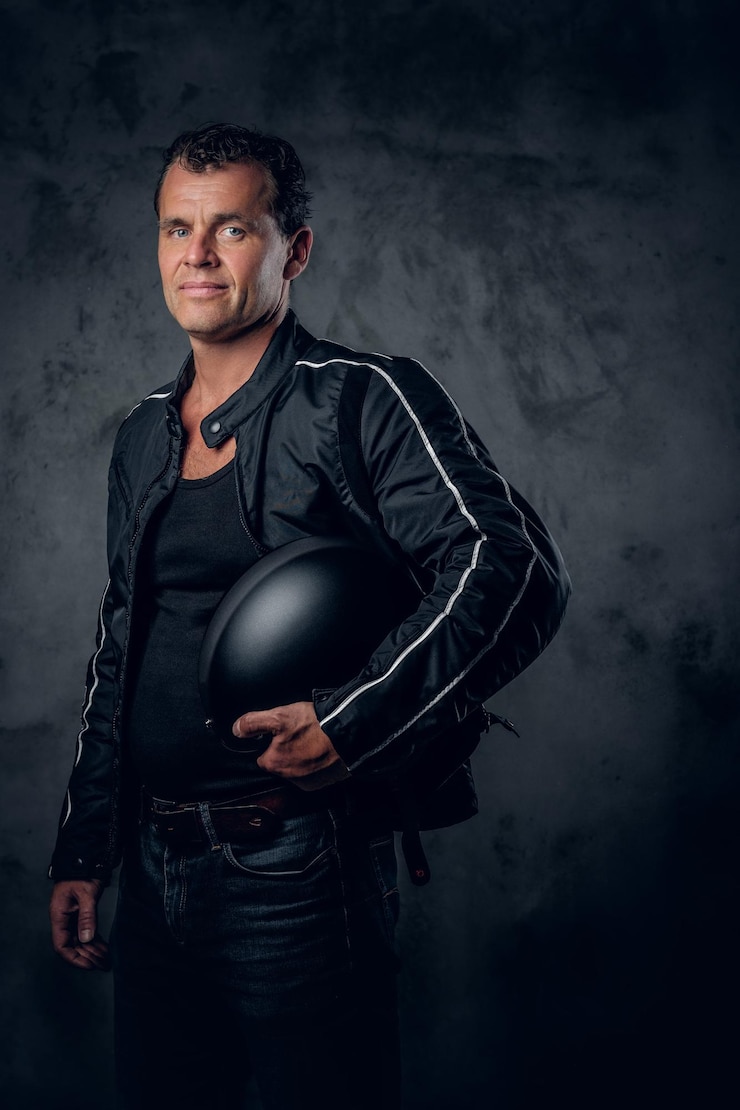 Foto grátis retrato de motociclista de meia idade na jaqueta esportiva, detém o capacete da motocicleta em fundo cinza.