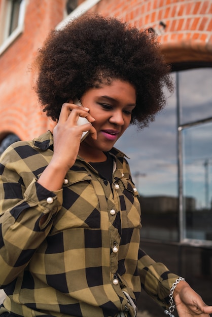 Retrato de mulher afro-latina falando ao telefone, ao ar livre na rua. Conceito urbano e de comunicação.