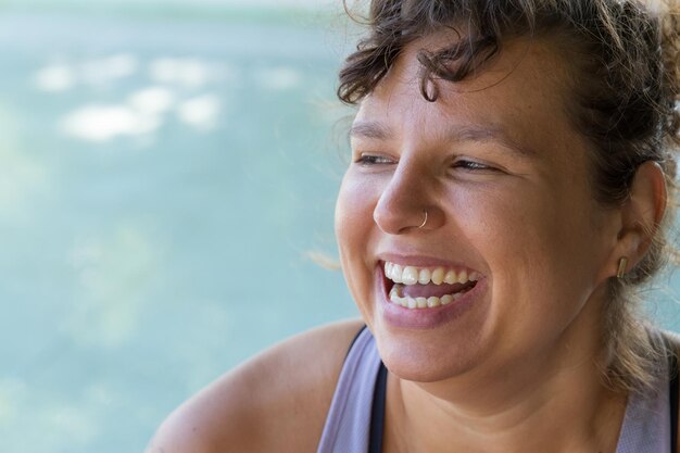 Retrato de mulher alegre com franja encaracolada. Mulher gordinha de top azul com piercing no nariz, sorrindo alegremente. Esporte, conceito positivo de corpo