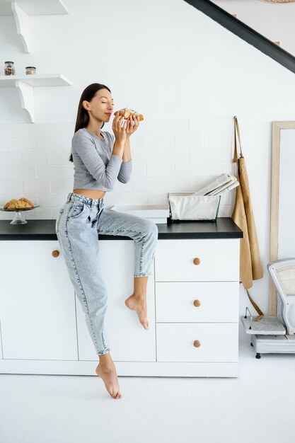 Retrato de mulher alegre come saboroso croissant em casa. Conceito de alimentos pouco saudáveis.