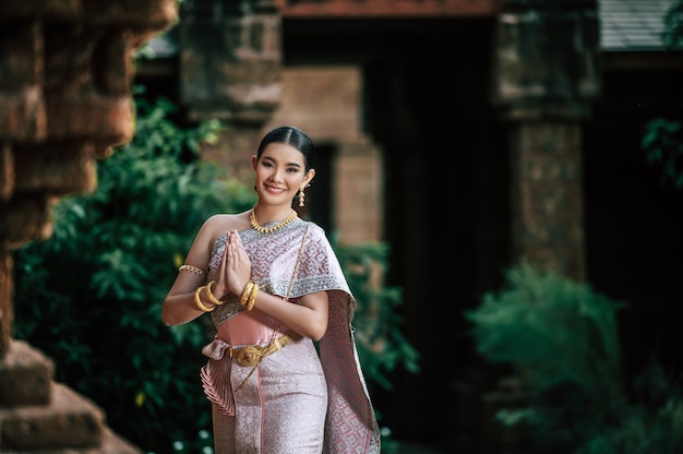 Retrato de mulher asiática encantadora usando um lindo vestido tailandês típico da cultura de identidade da Tailândia em um templo antigo ou lugar famoso com pose graciosa