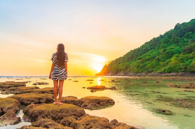 Retrato de mulher asiática na rocha ao pôr do sol ao redor do oceano nas férias