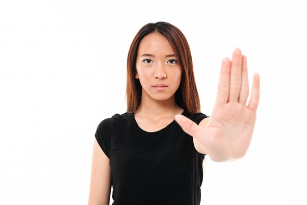 Retrato de mulher asiática séria em pé com a mão estendida, mostrando o gesto de parada