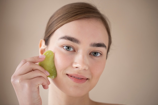 Retrato de mulher bonita com pele clara usando guasha para massagear o rosto