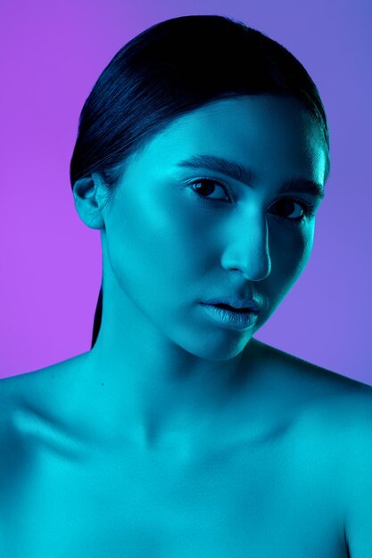 Retrato de mulher bonita isolado no fundo roxo do estúdio em luz de néon, monocromático. Lindo modelo feminino. Conceito de emoções humanas, expressão facial, vendas, publicidade, moda e beleza.