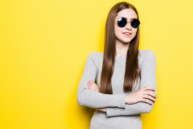 Retrato de mulher bonita sorridente em óculos de sol e vestido contra parede amarela