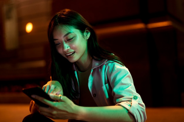 Retrato de mulher bonita usando smartphone à noite nas luzes da cidade