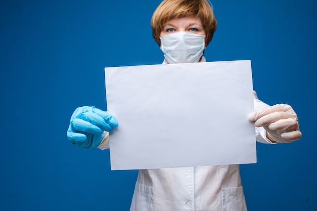 Retrato de mulher branca com cabelo curto loiro em um vestido branco médico, máscara e brilhos mostra uma folha de papel branca