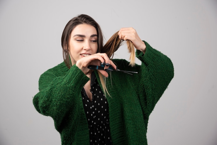 Foto grátis retrato de mulher com casaco verde, cortando o cabelo com uma tesoura.