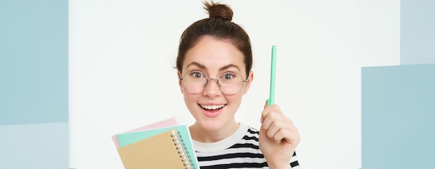 Foto grátis retrato de mulher com óculos tutor levanta a mão com caneta gesto eureka tem idéia ou solução detém